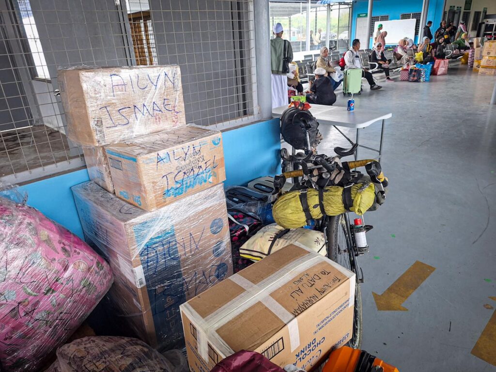 Loaded touring bicycle parked among boxes and luggage at a ferry terminal in Southeast Asia