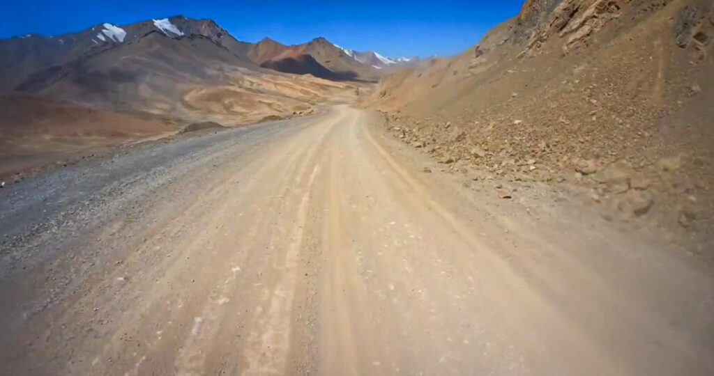 Gravel road on the Pamir Highway with snow-capped peaks in the distance