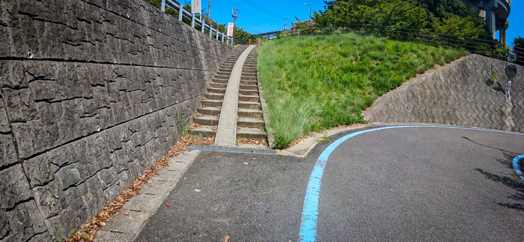 Steep stairs shortcut next to the curved bike ramp on the Shimanami Kaido, blue line marking the cyclist route