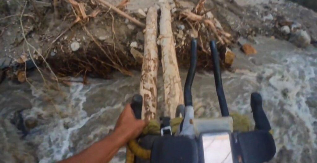 Bicycle crossing a makeshift log bridge over a river in the Wakhan Corridor after a landslide, Pamir Highway